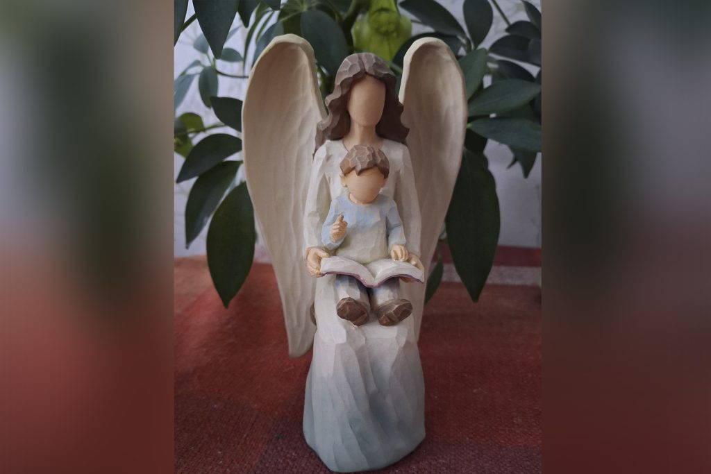 Pieni enkelifiguuri, jonka sylissä on lapsi lukemassa kirjaa.